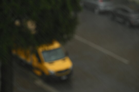Rainy day in a generic city, cars are visible but focus is on rain drops in the foreground.