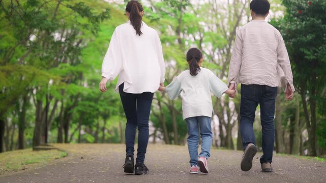 手を繋いで公園を歩く三人家族