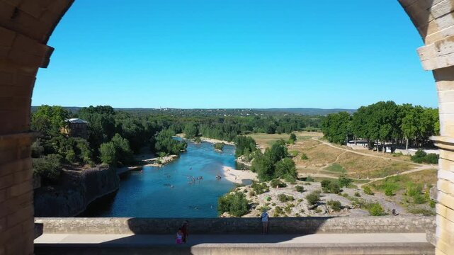 The Pont du Gard is an ancient Roman aqueduct, France, that is depicted on five euro note. A drone flies through a bridge arch. Summertime.