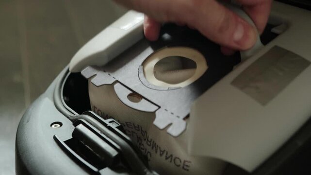 Person performing routine vacuum cleaner maintenance, opening appliance body to access empty space and internal filter, then carefully placing fresh dust bag into dedicated compartment.