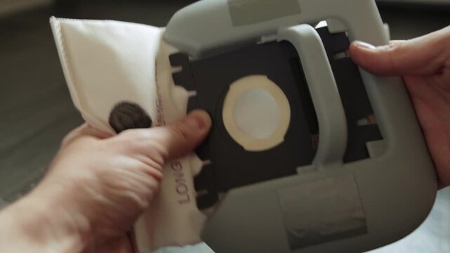 Detailed view of hands inserting new disposable dust bag into vacuum cleaner compartment. Action essential for routine appliance maintenance, promoting clean home, efficient operation.