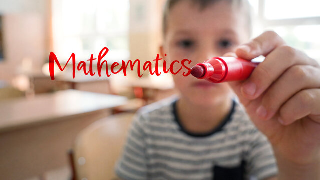 Young boy in classroom writing mathematics with red marker, focus on education and learning in school, childhood educational development concept