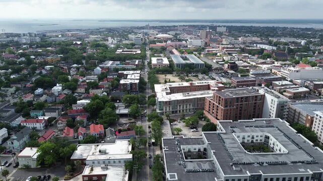 Central corridor sweep shows Meeting St multifamily buildings transitioning into historic residential blocks leading toward Cooper River waterfront. Varied roofing, foliage shape Charleston, SC