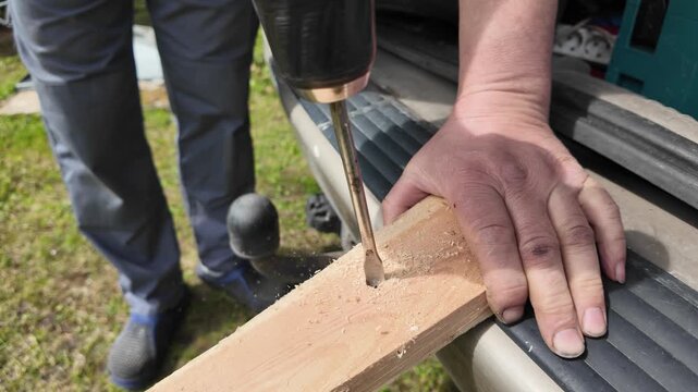 Close up of drilling hole in wooden board with cordless drill outdoors