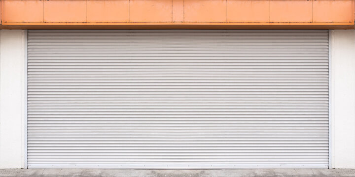 Front view of a closed metal roller shutter door of a shop with an orange top panel. Iron rolling garage gate background for business closure, store for rent, or secure storage concept.