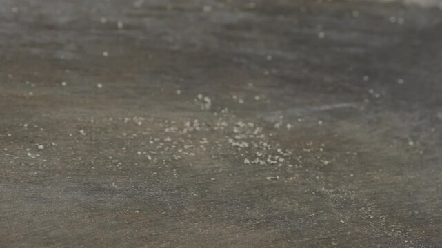 Worker sweeps scattered white recycled plastic granules across grey factory floor with broom in close up