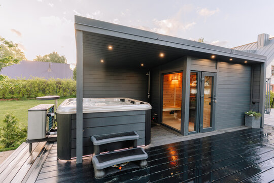 Modern outdoor spa with hot tub and wooden deck adjacent to a cozy cabin in a landscaped garden setting during sunset