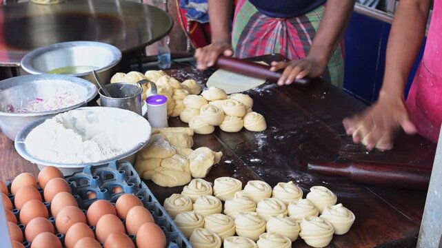 Close-up of street food vendors rolling and shaping dough spirals to prepare traditional parathas at an outdoor food stand in Bangladesh. Captures local culinary traditions and daily lifestyle.