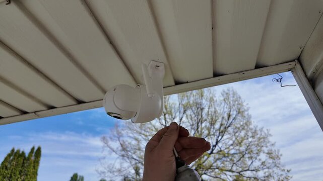 Removing outdoor security camera from house exterior with cordless screwdriver