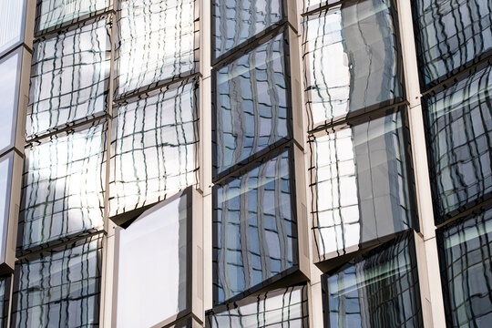 Reflective glass facade distorts neighboring building lines, where white panels, windows and urban architecture create abstract depth