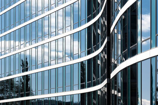 Glass facade curves across blue sky, where reflections, white bands and urban architecture form abstract office building lines in daylight