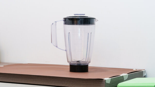 Transparent kitchen blender with black lid placed on a wooden countertop, surrounded by a clean, minimalistic kitchen environment featuring light-colored walls