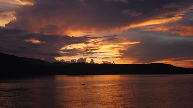 Vibrant sunset over Riung Bay and the 17 Islands Marine National Park, Flores, Indonesia, with traditional boats on calm water beneath dramatic orange, gold, and purple clouds