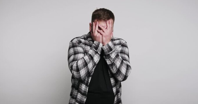 Young man reacts by covering his face while showing emotions in a simple setting