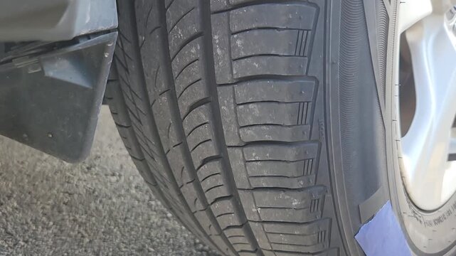 Video footage showing a screw embedded in the tread area of a passenger vehicle tire. Automotive maintenance footage illustrating puncture detection, tire inspection, wheel safety evaluation, and repa
