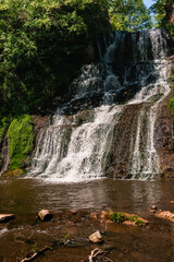 Fototapeta premium A tranquil Ukrainian waterfall descending over rugged stone terraces, bordered by dense trees and reflecting the beauty of untouched nature.