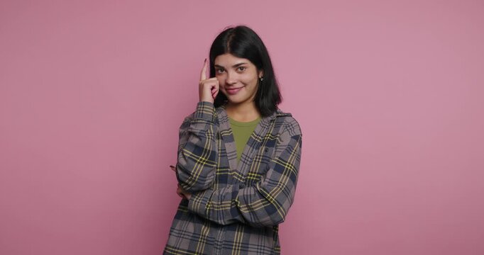 Smiling woman posing in front of pink background while using mobile phone in indoor space