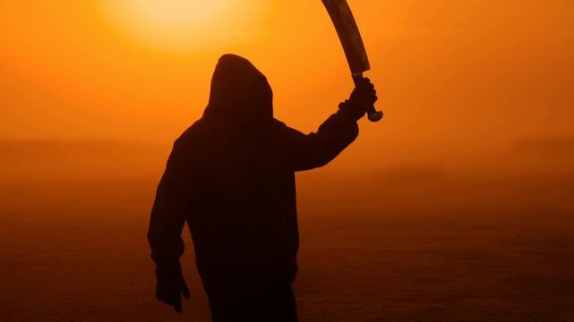 Hooded figure wielding machete in dramatic sunset silhouette sequence