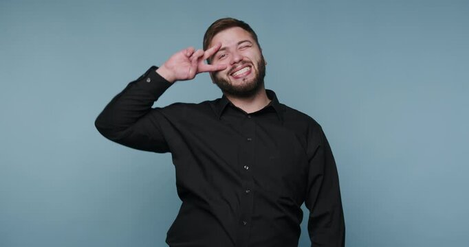 Man makes fun faces and poses in front of blue background during indoor photoshoot