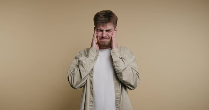 Young man experiences discomfort while holding his head and showing signs of stress in a simple room setting