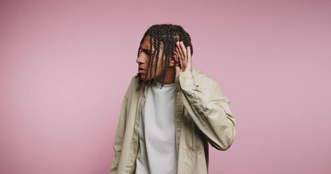 Man listens closely in a studio with pink background while showing curiosity and focus in different frames throughout the clip