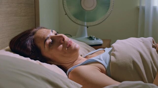 Menopausal woman experiencing insomnia with fan in bedroom