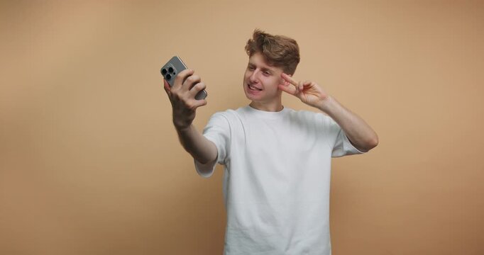 Young man takes selfies in a simple indoor setting with a plain background while showing different poses and expressions