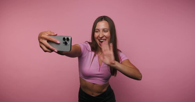 Smiling girl takes selfies and shows her fun side in a bright pink background