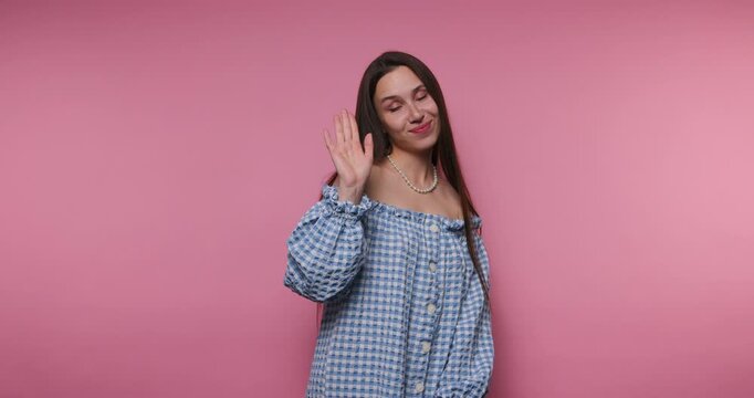 Smiling woman waves at camera in a pink room during a photo session in the afternoon light