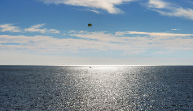Parasailing over sparkling sea with blue sky and copy space. Sun glitter on calm sea horizon with blue sky and copy space
