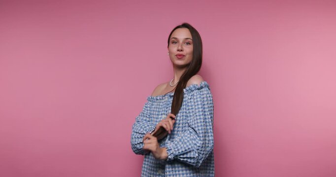 Woman with long hair shares styling tips against a pink background while posing and smiling