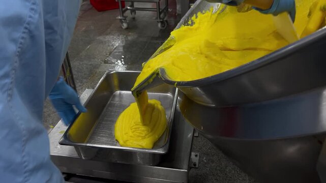 Prepared food filling being transferred from an industrial mixing kettle into containers for weighing and batch control. Food manufacturing process supporting product consistency, quality assurance, a