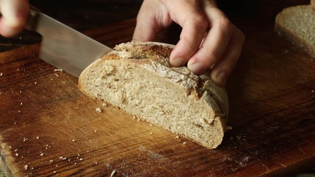 Hands slicing of loaf of homemade whole grain bread