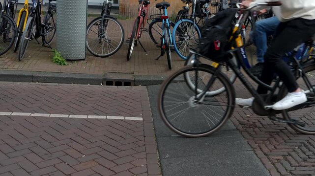 Street view of bike riders passing by in Amsterdam on a street, you can only see the legs and wheels on a cloudy spring day