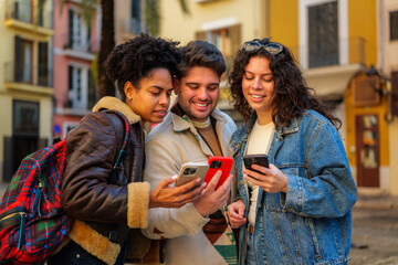 Group of young diverse friends smiling and sharing content on their mobile phones while traveling...