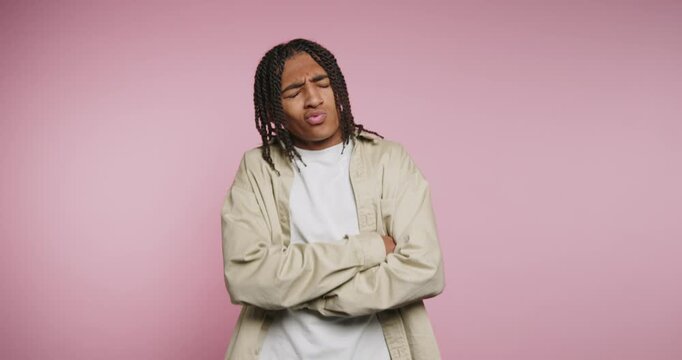 Young person stands with arms crossed and expresses emotions in a studio with pink background in a casual outfit