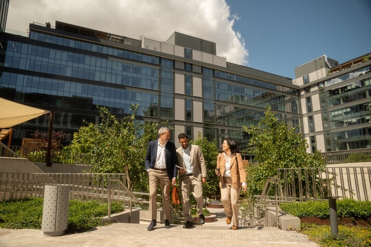 Corporate employees chatting and laughing as they leave the office after work on a sunny day
