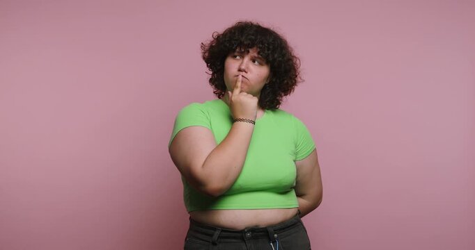 Woman poses with a thinking expression against a pink background in a studio setting in the afternoon