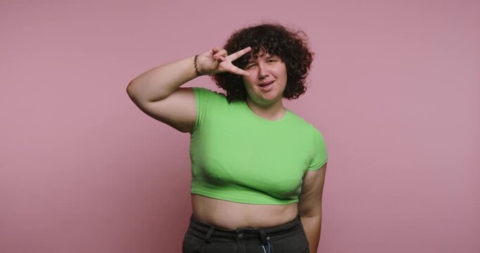 Person shows different hand signs and smiles against a pink background while wearing a green shirt