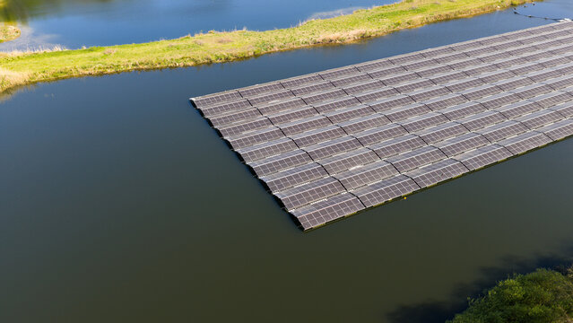 Aerial view of a floating solar farm with rows of photovoltaic panels on a calm lake surrounded by green grassy banks in Zwolle, Overijssel, Netherlands.