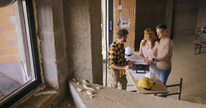 Construction worker showing the progress of a house build to an adult couple at the construction site.