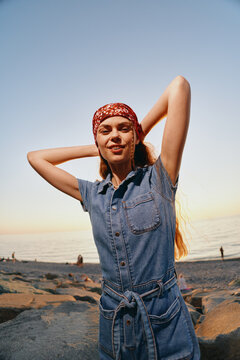 lifestyle woman in modern boho-western denim outfit posing on beach at sunset with relaxed expression and film color tones, stylish street style vibe
