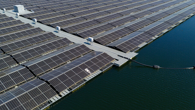 Aerial view of a large floating solar farm with rows of photovoltaic panels on a calm lake under a clear blue sky in Zwolle, Overijssel, Netherlands.