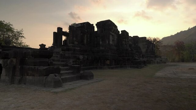Tilt up shot revealing Prasat Hong Nang Sida against a warm orange sunset sky at the Wat Phou archaeological complex in Champasak, Laos.