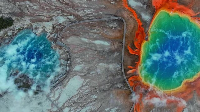 Boardwalk walk way trail Midway Geyser Basin two vibrant turquoise hot springs pool Grand Prismatic Spring birdseye aerial drone Yellowstone National Park Wyoming volcanic thermal hot steam upwards