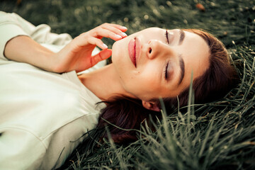 Fototapeta premium Young woman relaxing with eyes closed while lying in grass outdoors enjoying a peaceful natural moment