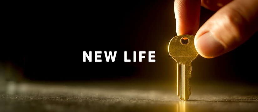 Hand holding golden key on dark background with New Life text, concept of hope, future and new beginning