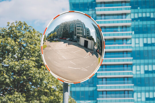 Convex mirror providing a wide angle view of a city intersection, reflecting a contemporary glass building and parked cars