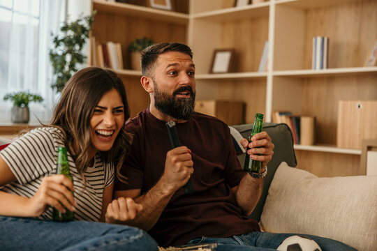 Couple cheering, watching exciting sports game at home
