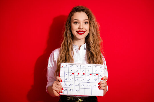 Young woman holding calendar marked with key dates, wearing white shirt on red background, symbolizing planning and organization